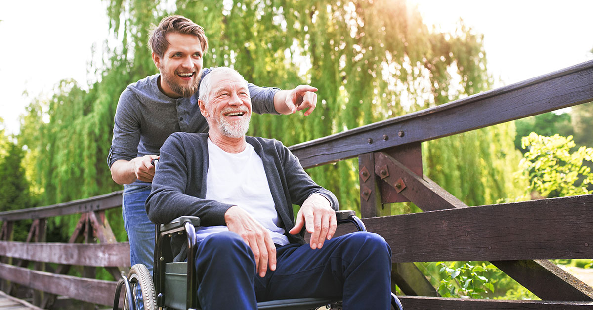 Senior im Rollstuhl mit seinem Pfleger im Freien bei einem Spaziergang